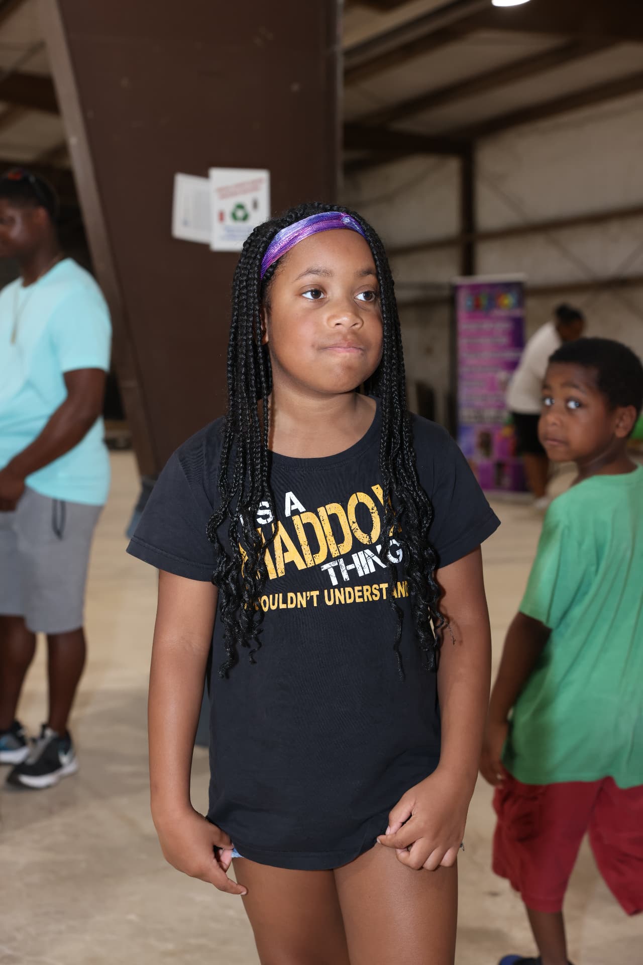 A young girl at the festival with children playing in the background.