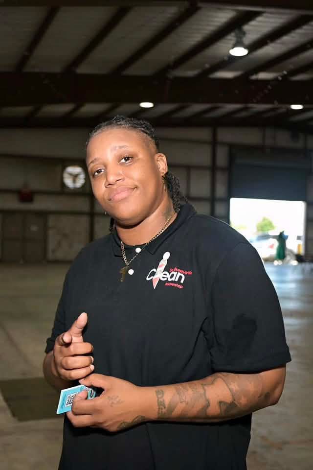 A So Fresh-N-So Clean Barbershop volunteer smiling and pointing at the camera.