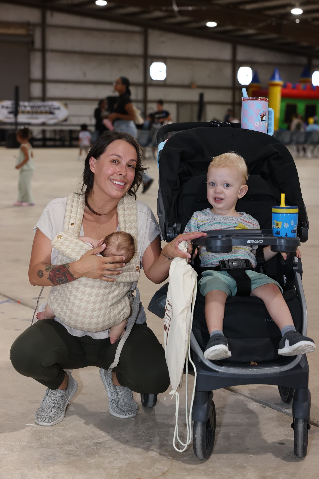 A mother with her baby and toddler in a stroller near the bounce houses.