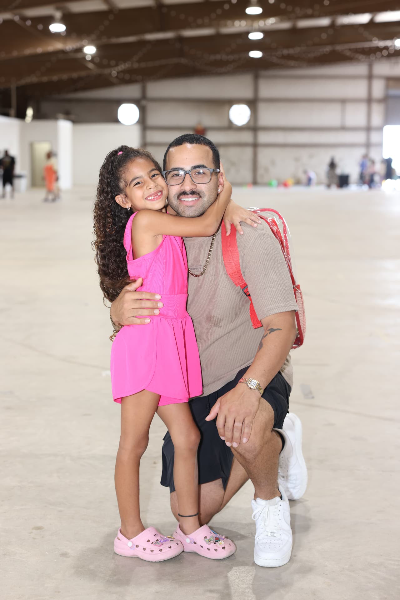 A father kneeling with his daughter, who wears a clear backpack.