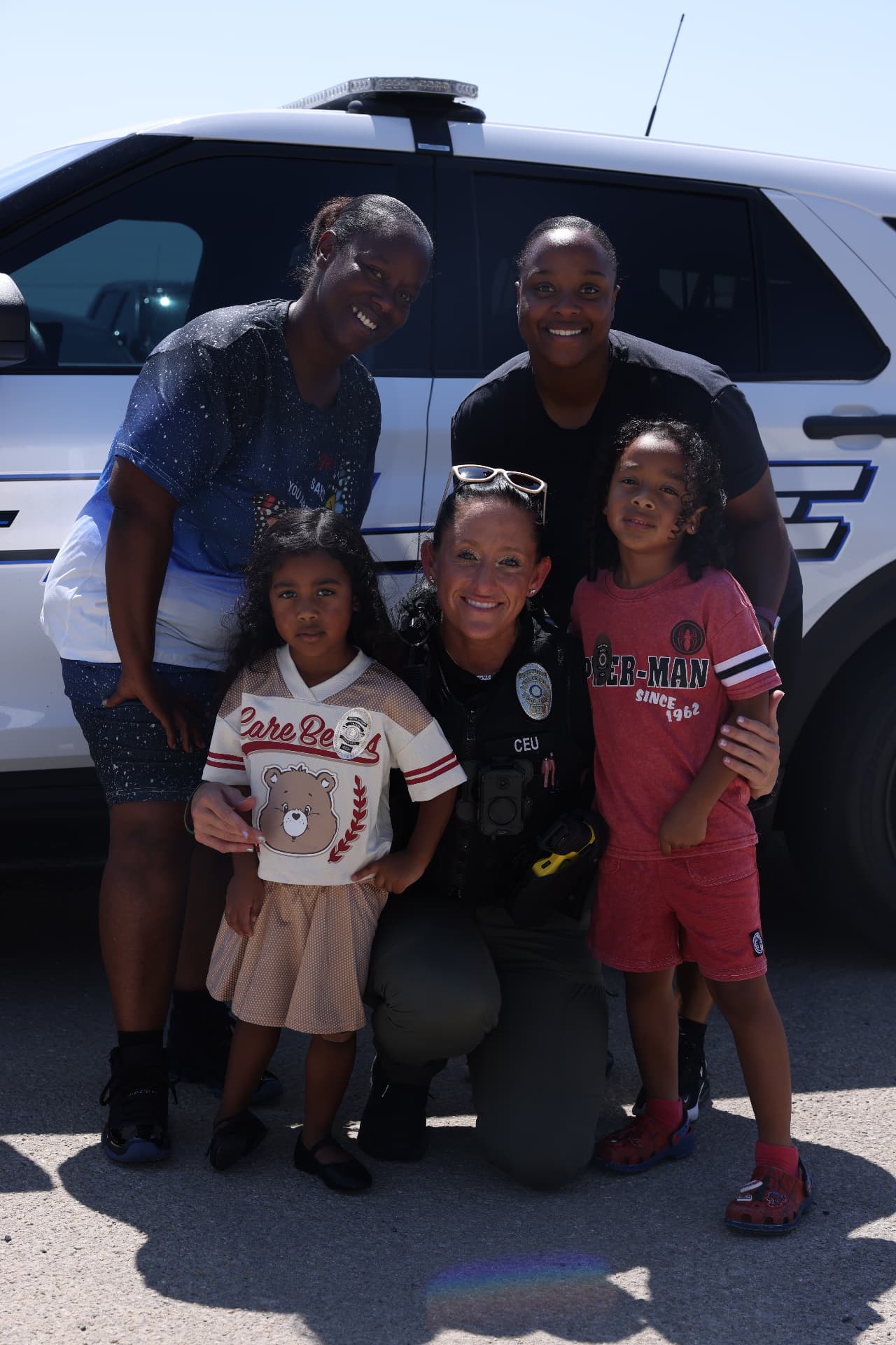 A police officer posing with a family and children beside a patrol vehicle.