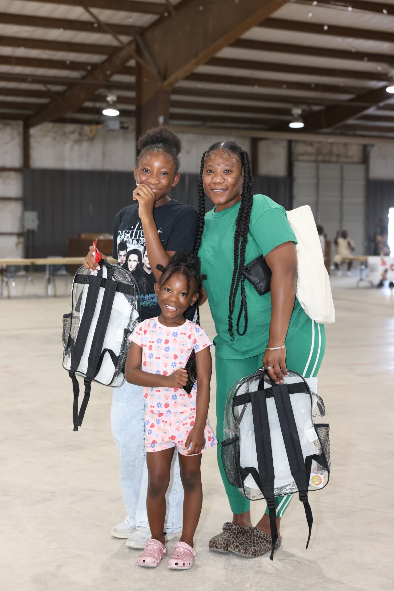 A mother and her two daughters holding clear backpacks they received.
