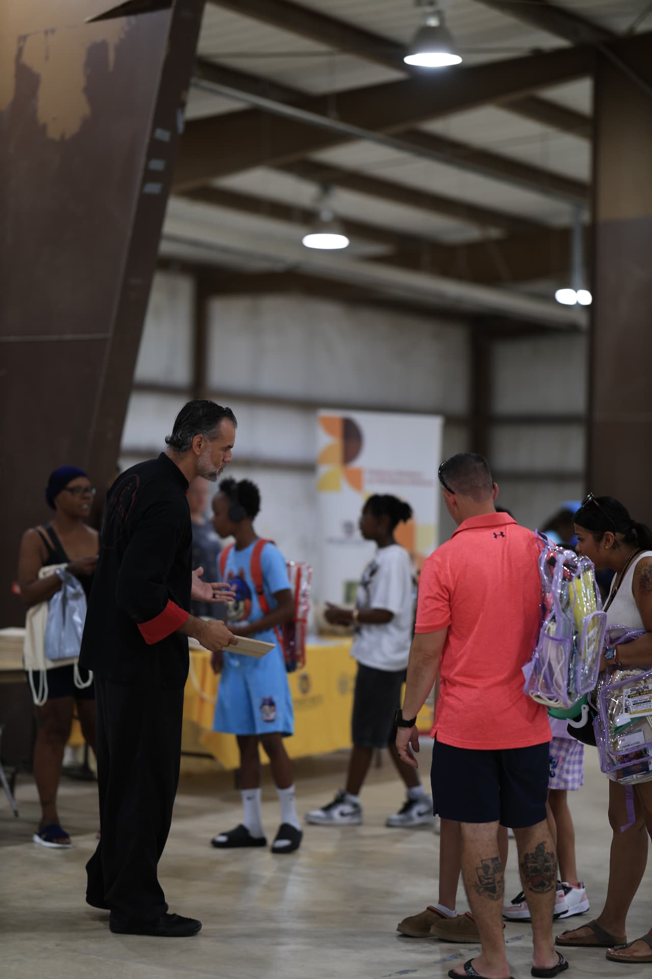 A partner handing out information as families carry clear backpacks through the hall.