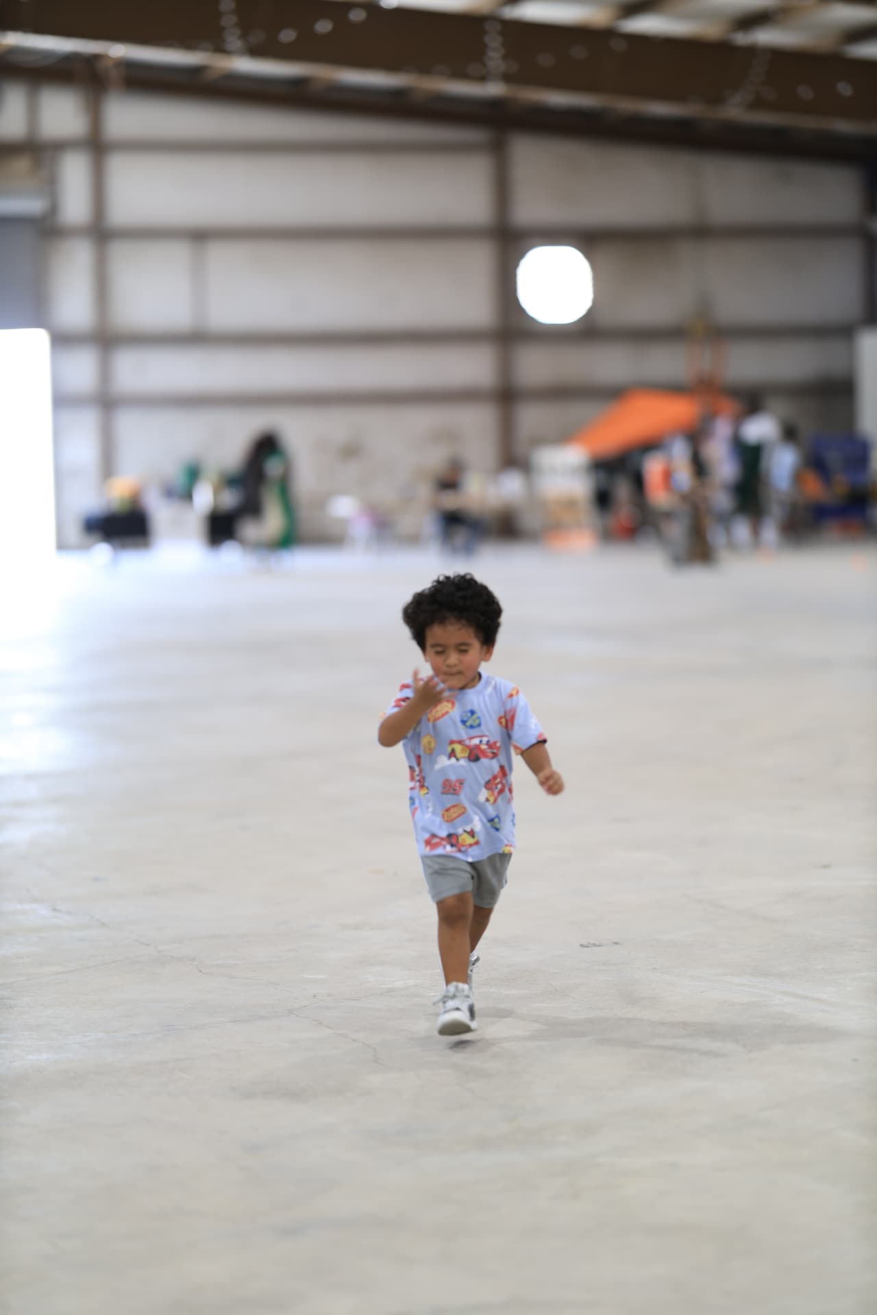 A young boy in a Cars t-shirt running across the open festival floor.