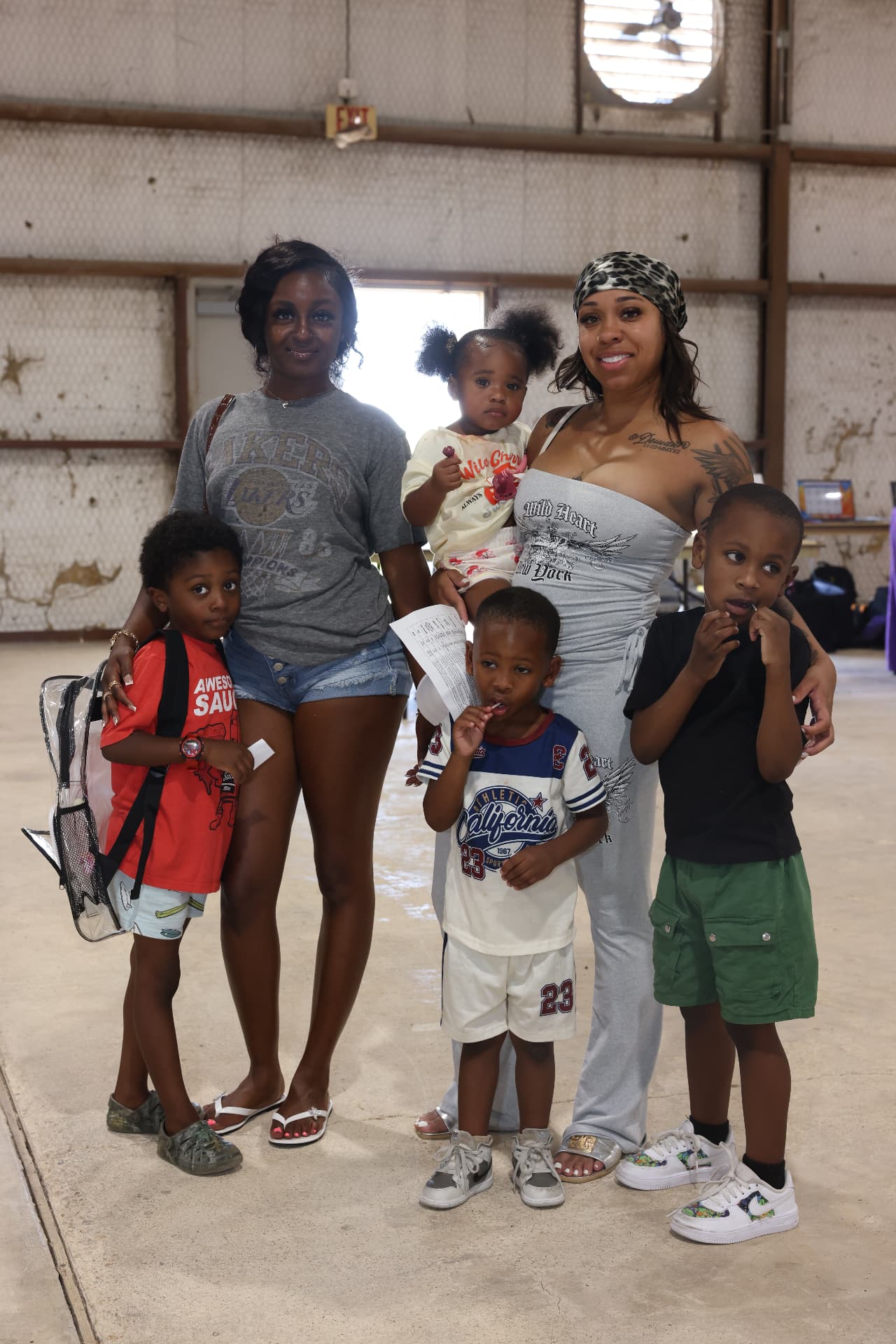 Two mothers with four children, one wearing a clear backpack, posing together.