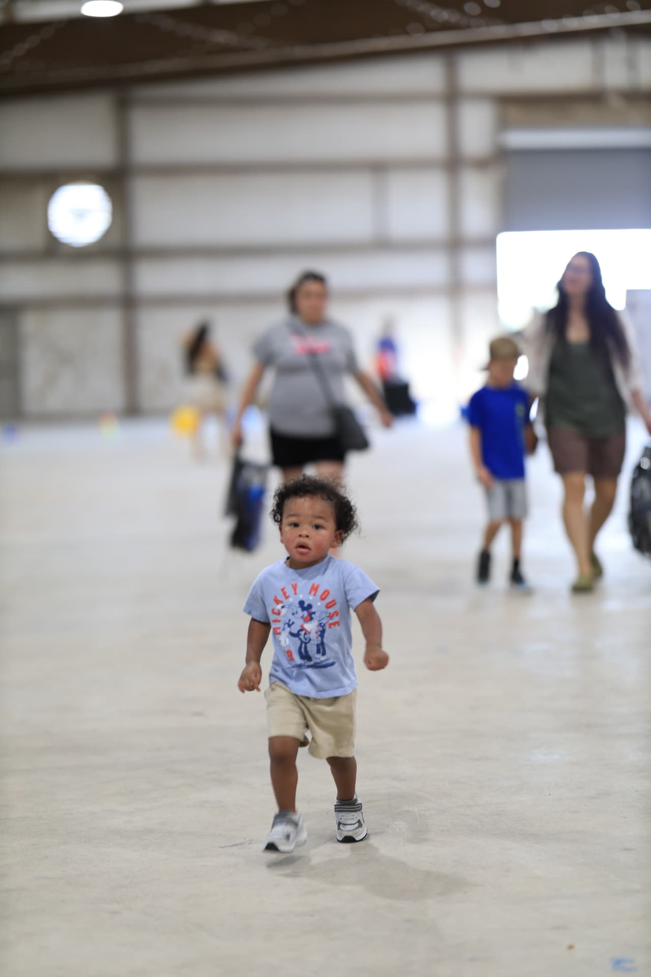 A toddler running across the venue floor as families arrive.