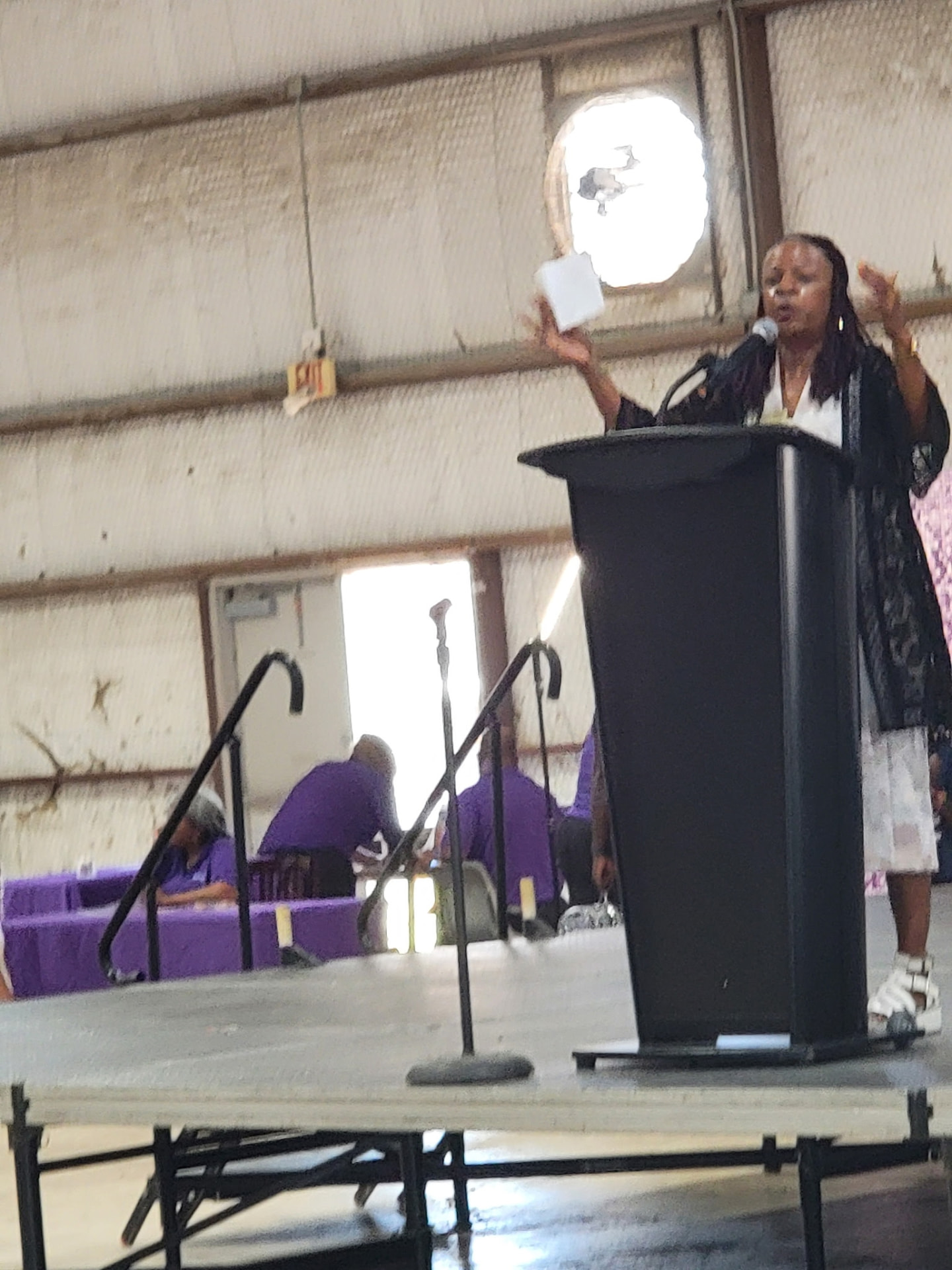 A speaker addressing the crowd from the podium with partner tables behind her.
