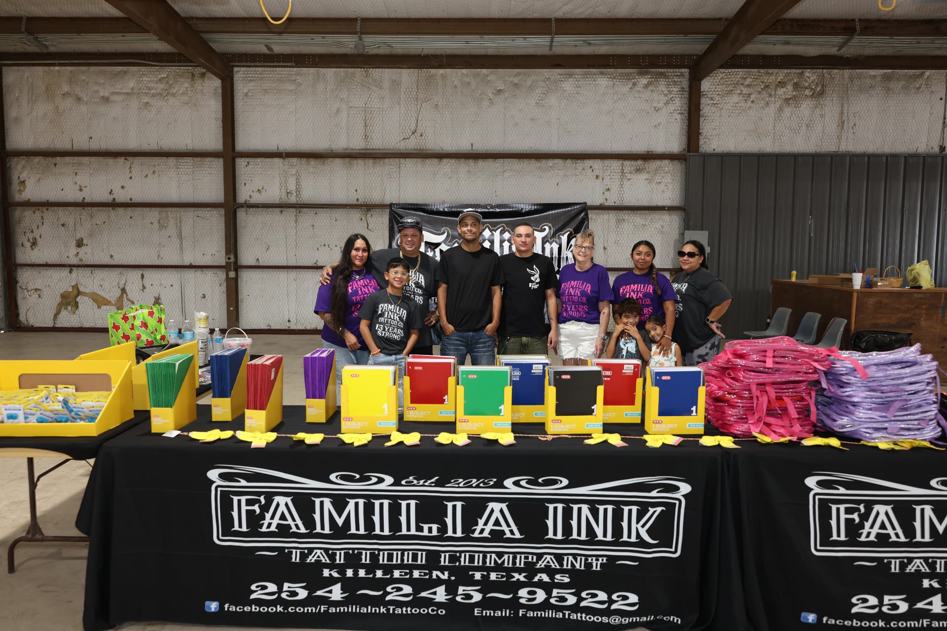 The Familia Ink Tattoo Co. team behind a table of school supplies and clear backpacks.