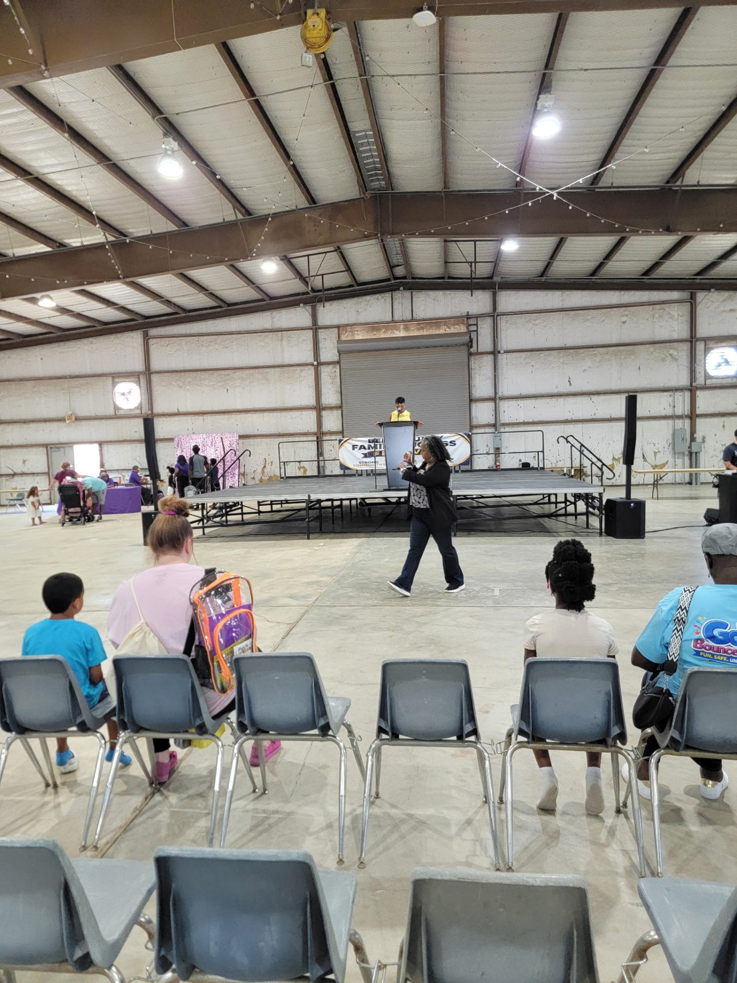 Families seated in front of the stage, a child wearing a clear backpack.