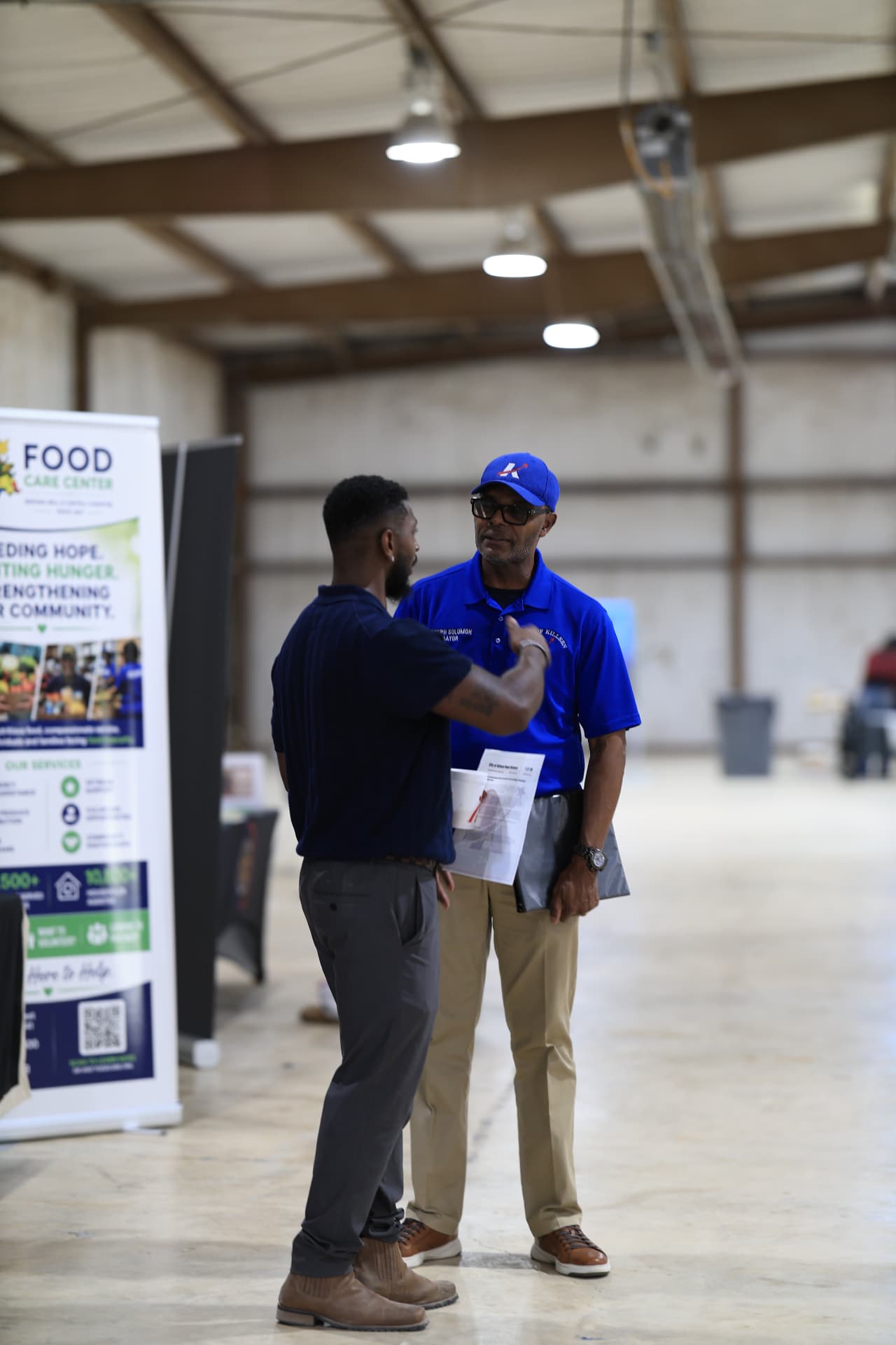 The festival organizer talking with Mayor Joseph Solomon beside the Food Care Center banner.